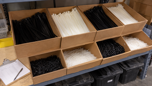 Contractor supply shelf with multiple large bulk boxes of zip ties and a purchase order clipboard