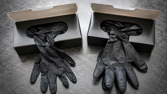 Two open boxes of black nitrile gloves side by side, one thinner and one thicker