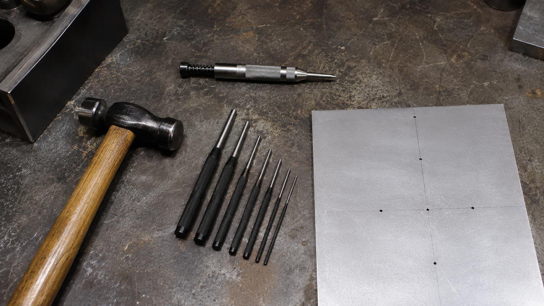Metalworking workbench with a center punch, a set of pin punches, a hammer, and marked sheet metal