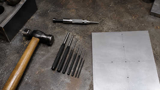 Metalworking workbench with a center punch, a set of pin punches, a hammer, and marked sheet metal